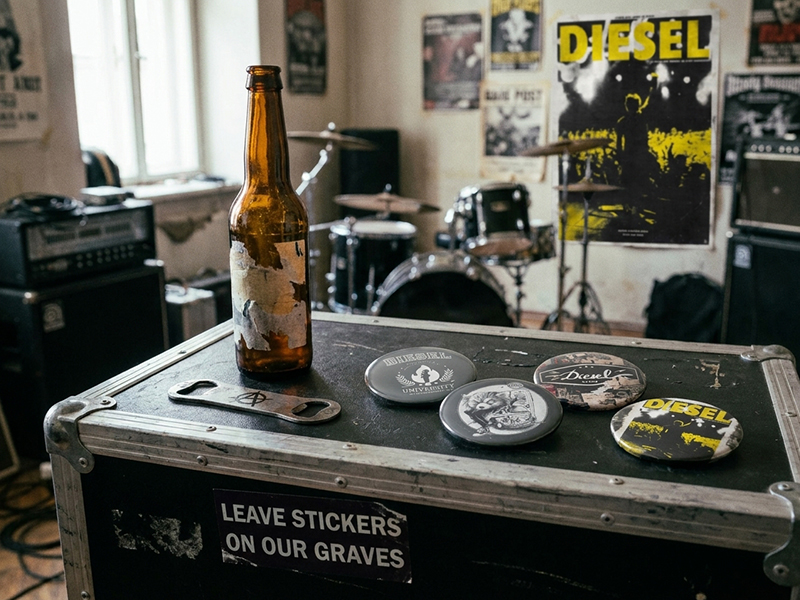 Décapsuleur punk, badges DIESEL et bouteille sur une caisse de matériel dans une salle de répétition rock. poster du film Diesel